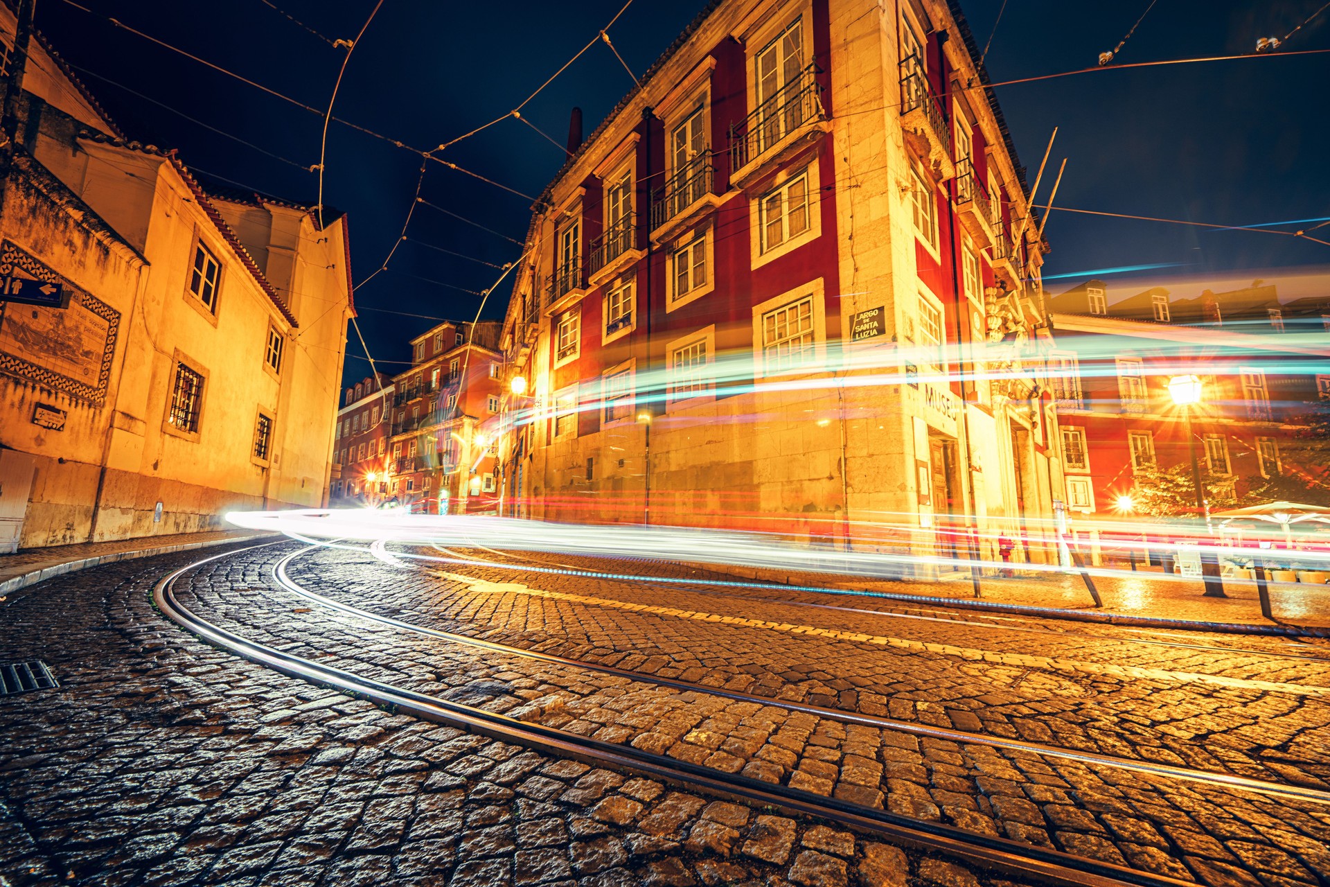 Tradicional rua antiga à noite iluminada com trilhos de eléctrico em Lisboa. Distrito de Alfama. Portugal.